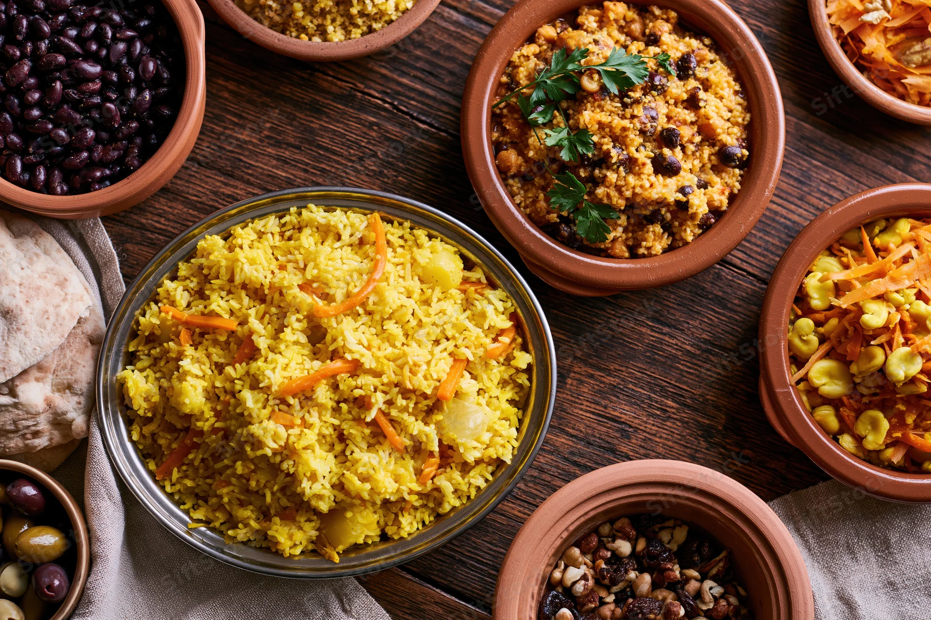 Overhead flat lay of a middle eastern and north african meal spread with rice, couscous, beans, vegetables and bread on a wooden table