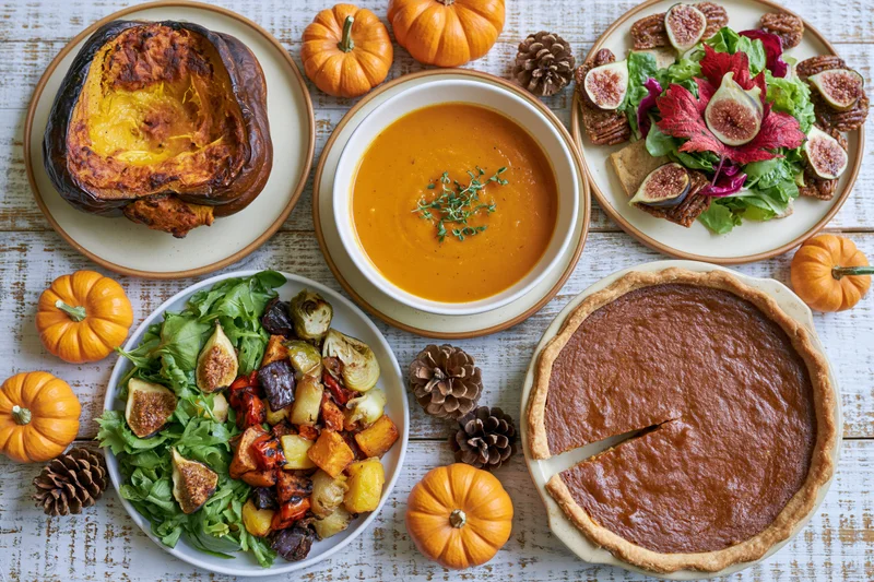 Thanksgiving meal spread with pumpkin pie, soup, salads and decorative gourds on whitewashed wooden table