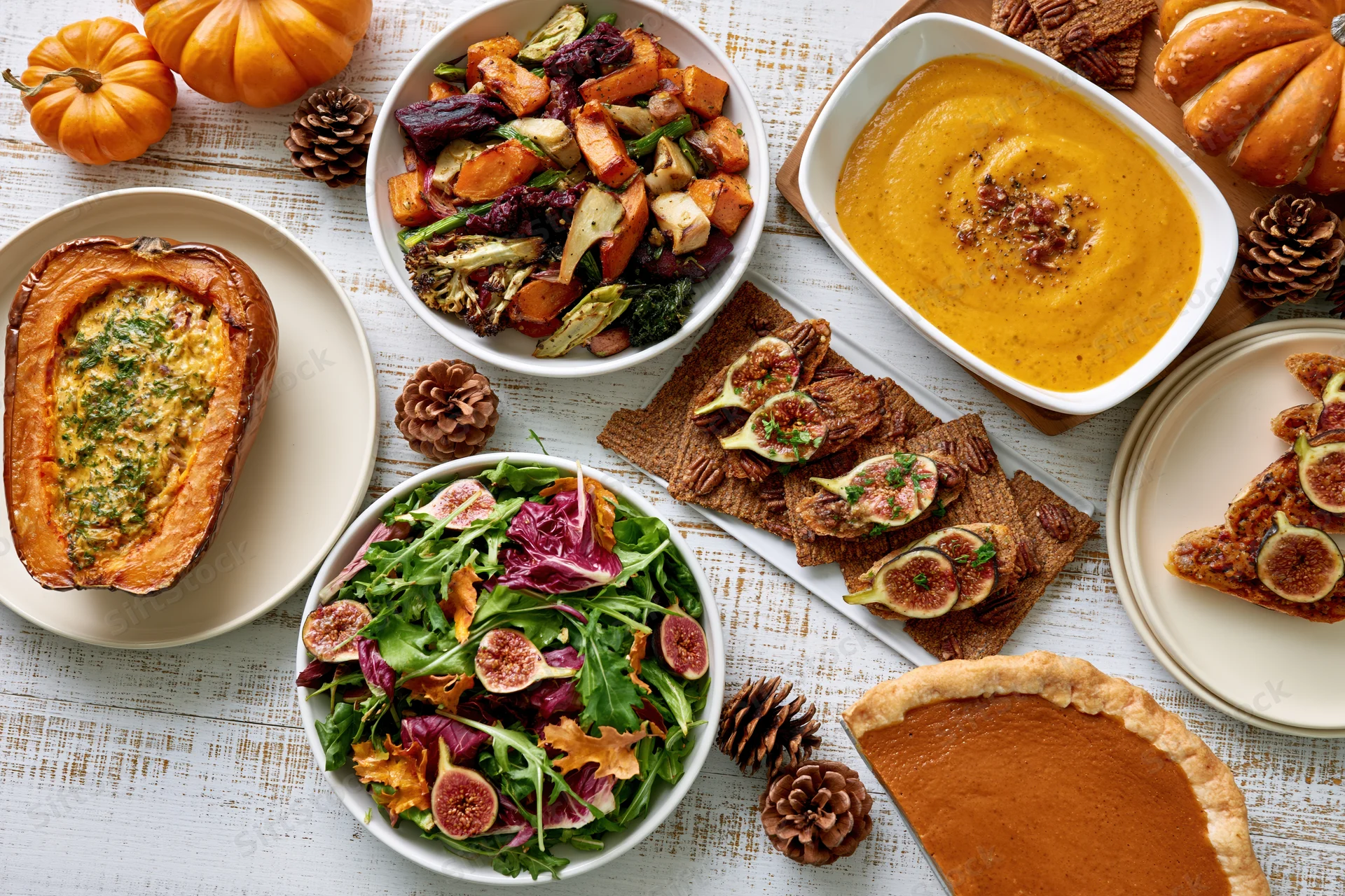 Overhead flat lay of a thanksgiving feast with pumpkin dishes, salad, pie, and autumn decorations on a whitewashed wooden table