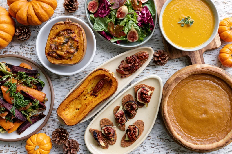 Overhead flat lay of thanksgiving dishes including pumpkin pie, soup, salad, and roasted vegetables on a whitewashed wooden table