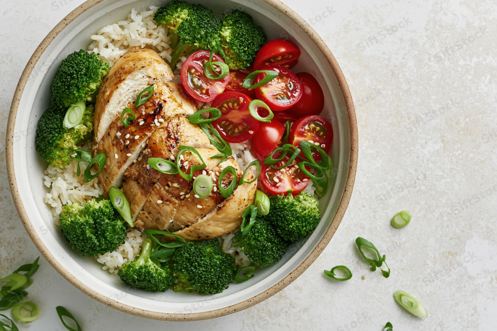 Grilled chicken with rice, broccoli, cherry tomatoes and green onions in a ceramic bowl, overhead view