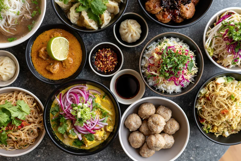 Overhead flat lay of diverse asian dishes arranged on a dark stone table