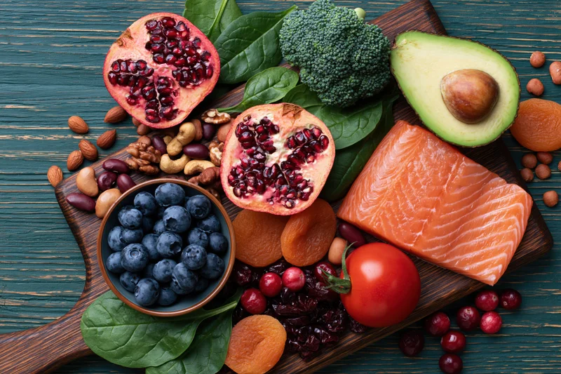 Salmon and avocado with pomegranate, blueberries, broccoli, and nuts arranged on a dark wooden cutting board in overhead flat lay