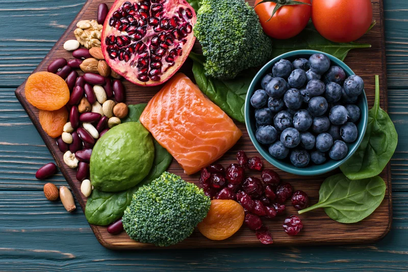 Salmon and vegetables arranged on a dark wooden cutting board with fruits and nuts