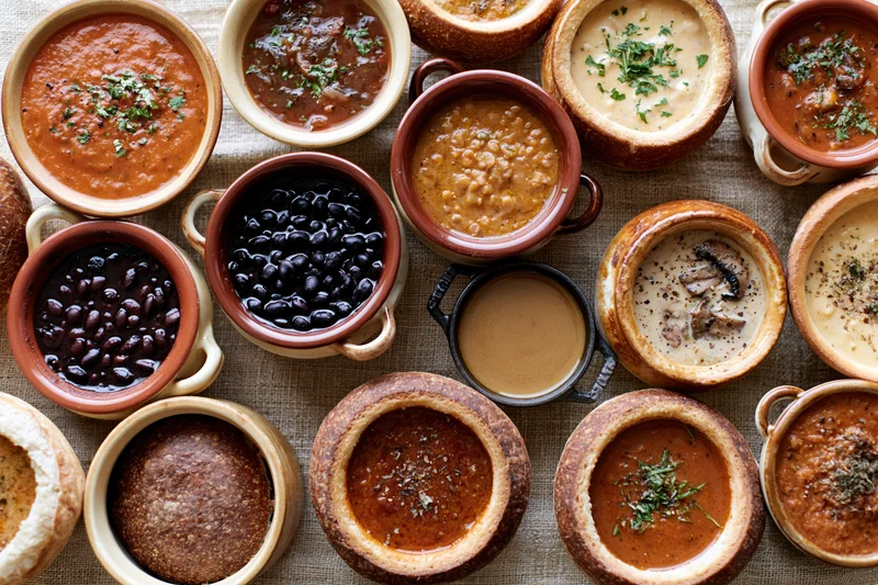 Overhead flat lay of assorted soups and stews in ceramic bowls on a linen tablecloth
