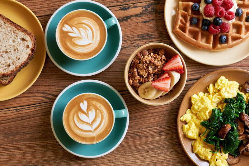 Overhead view of a brunch spread with coffee, waffles, toast, and scrambled eggs on a wooden table