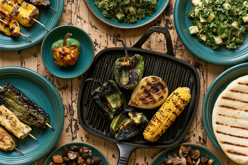 Grilled vegetables arranged on a cast iron skillet and teal plates on a rustic wooden table