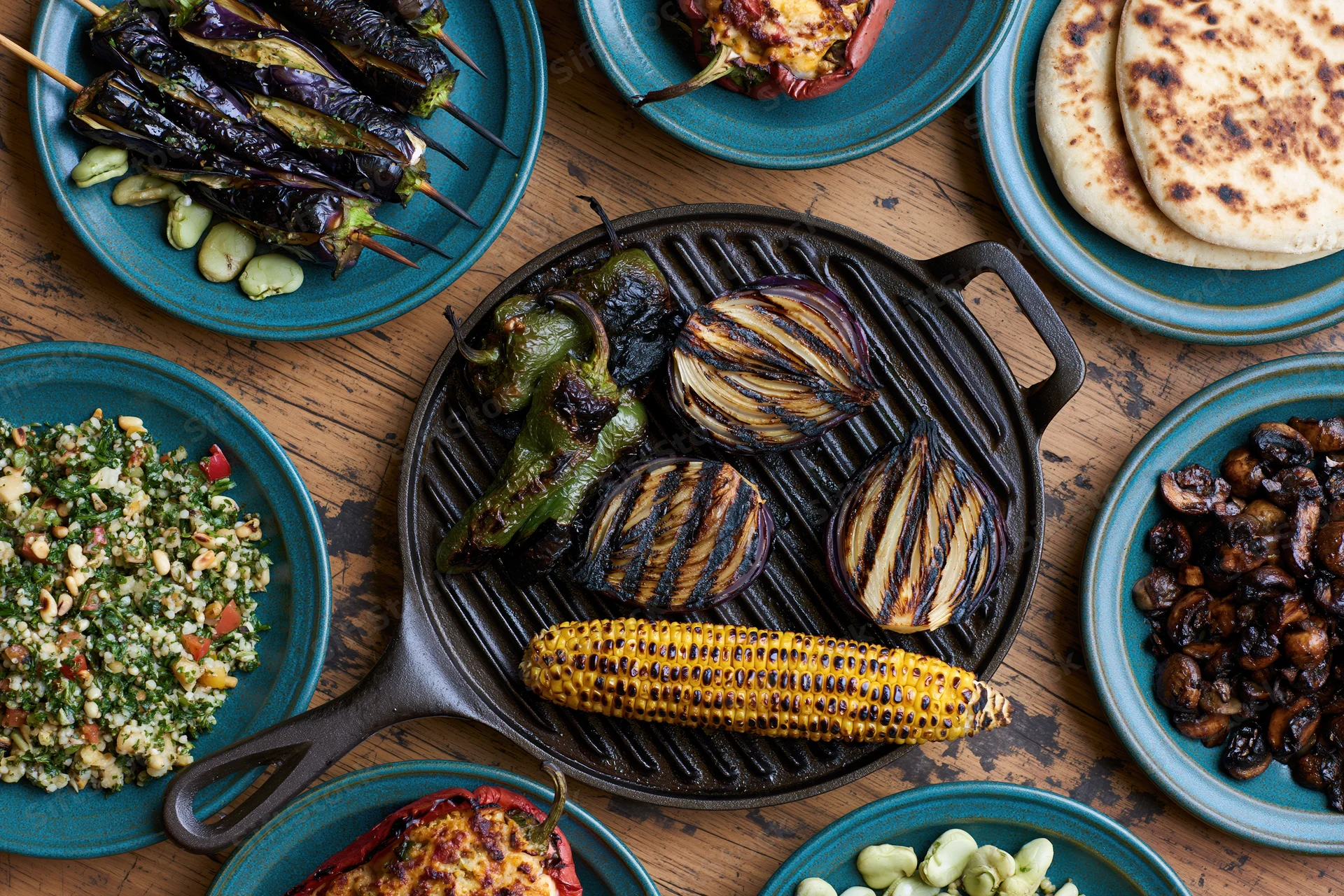 Grilled vegetables arranged on a cast iron skillet and teal plates on a wooden table