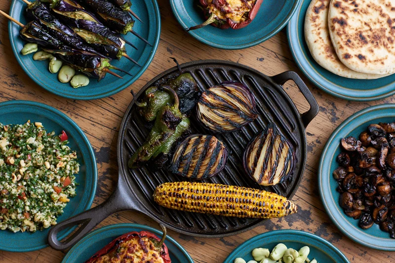 Grilled vegetables arranged on a cast iron skillet and teal plates on a wooden table