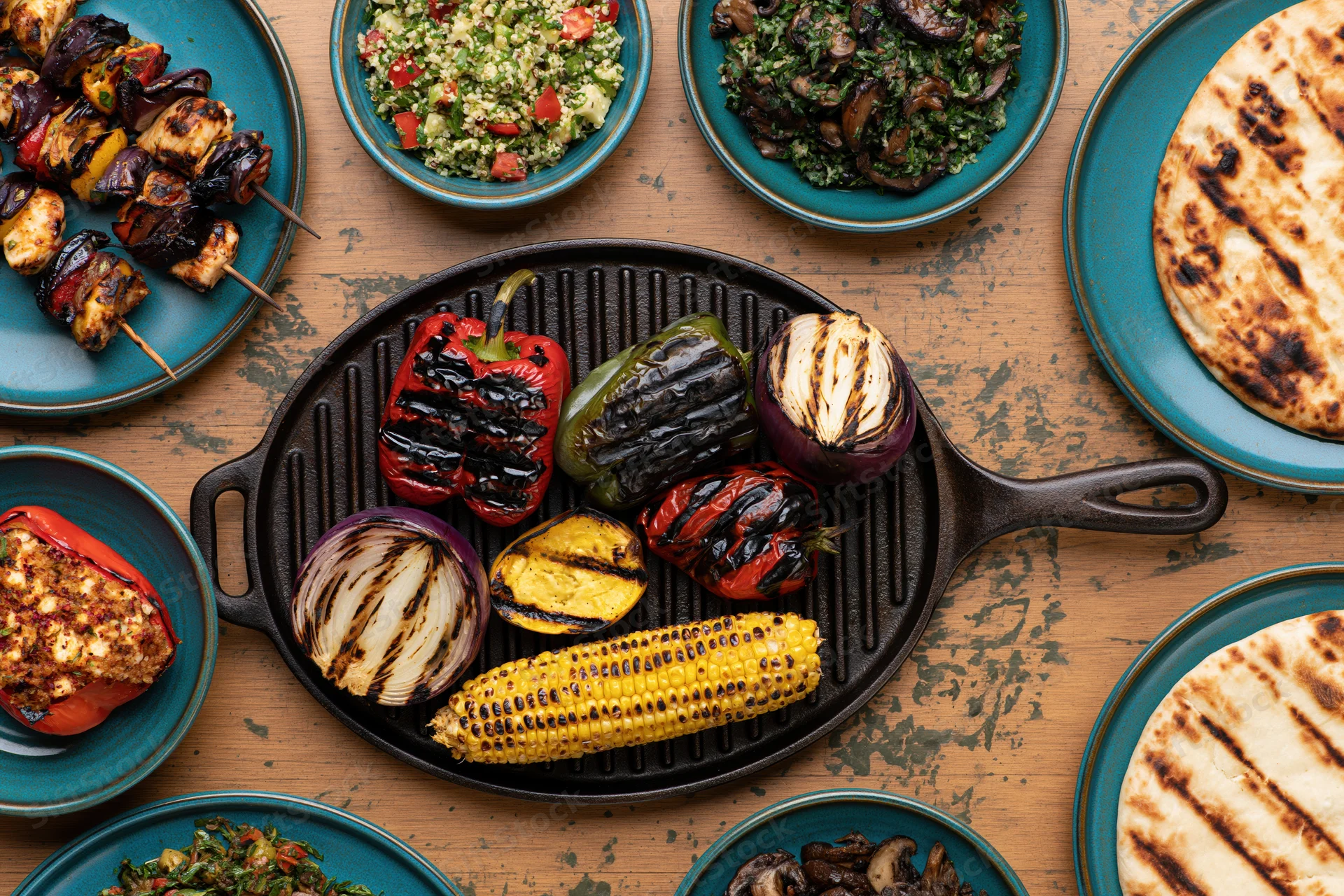 Grilled vegetables arranged in a cast iron skillet with side dishes on a wooden table