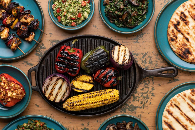 Grilled vegetables arranged in a cast iron skillet with side dishes on a wooden table