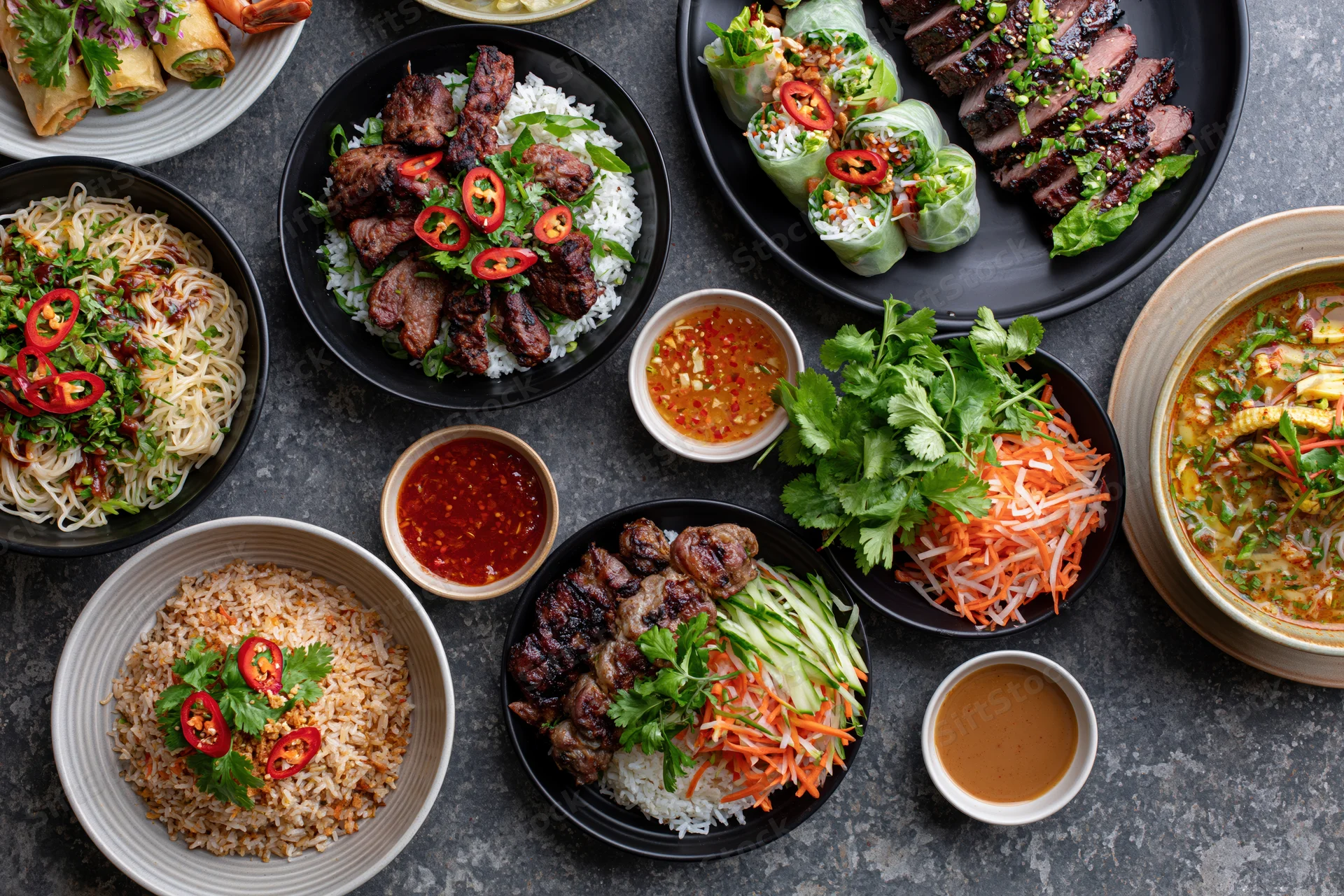 Overhead flat lay of a large spread of southeast asian dishes on a dark stone table