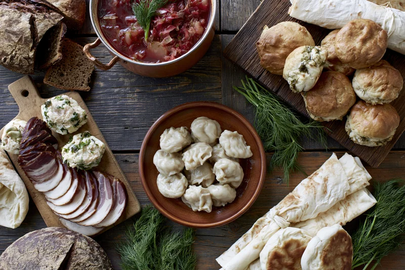 Traditional eastern european meal with borscht, dumplings, bread and herbs arranged on dark wooden table in overhead flat lay