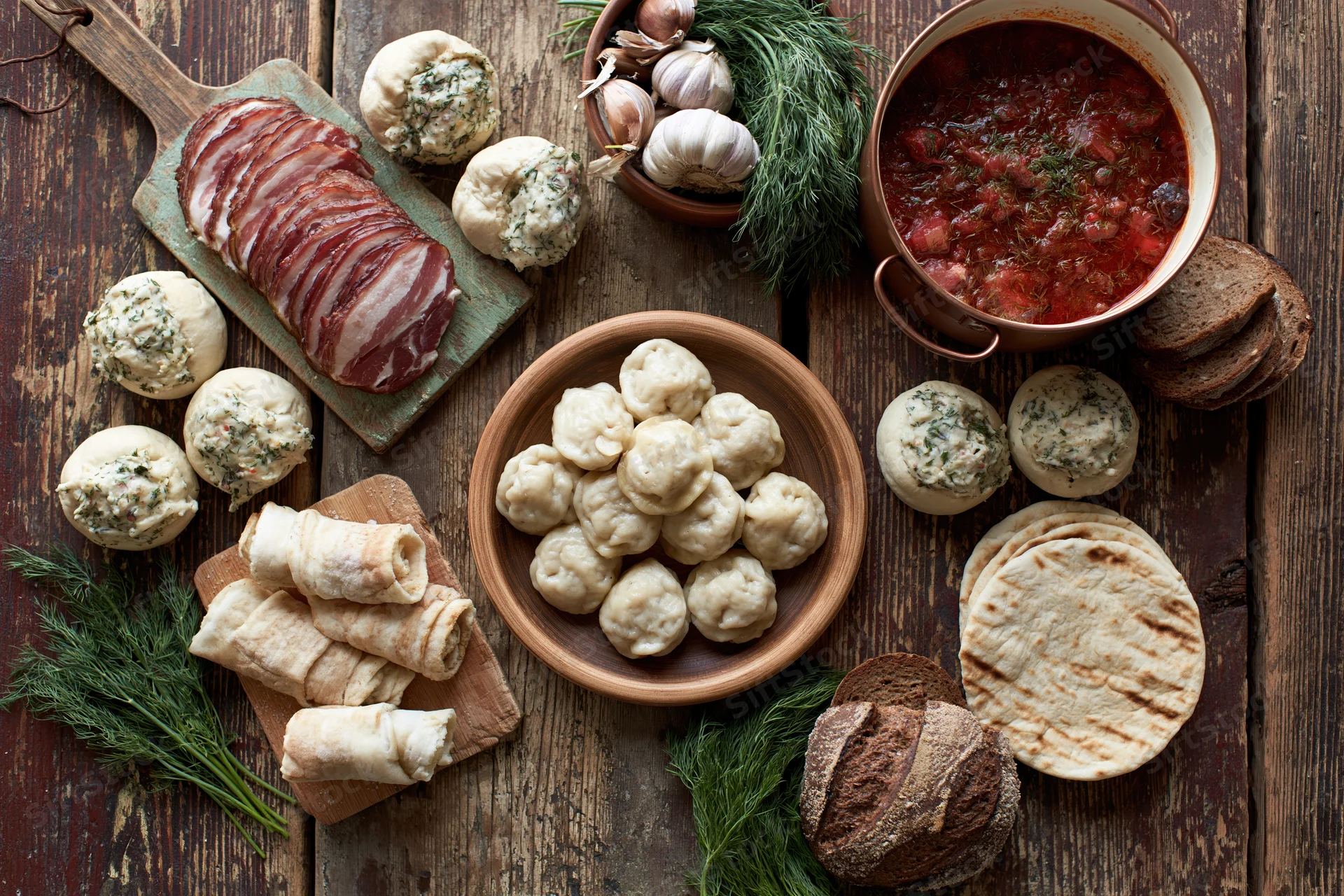 Traditional eastern european meal with dumplings, borscht, bread, and herbs arranged on a rustic wooden table in overhead flat lay