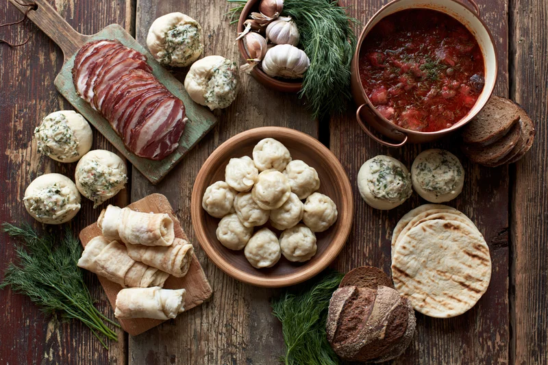 Traditional eastern european meal with dumplings, borscht, bread, and herbs arranged on a rustic wooden table in overhead flat lay