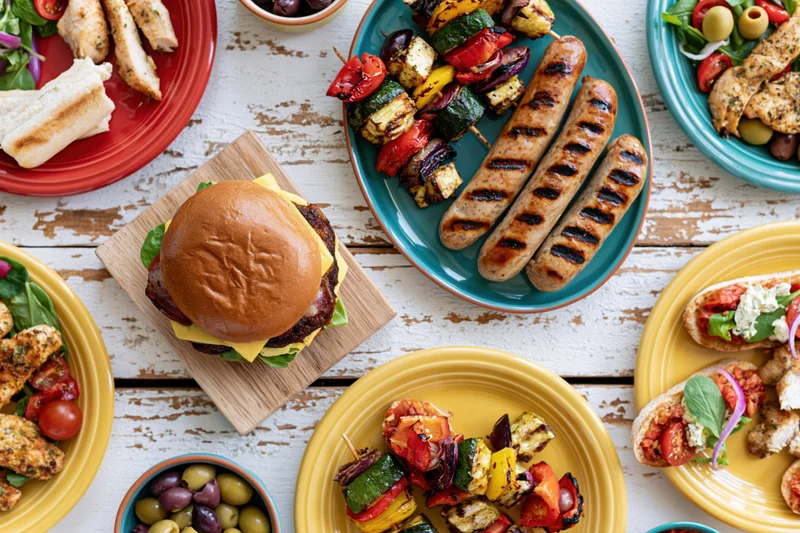 Overhead view of a summer barbecue spread with grilled sausages, burgers, kebabs and salads on a white wooden table
