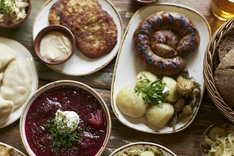 Traditional eastern european meal spread with borscht, sausage, pierogi, and bread on wooden table