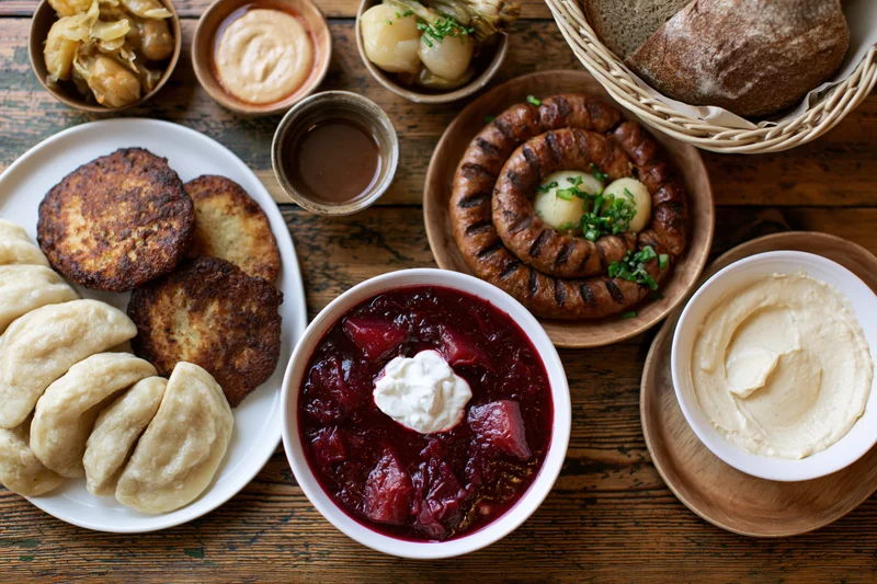 Traditional eastern european meal spread on wooden table with pierogi, fritters, bread, and sauces