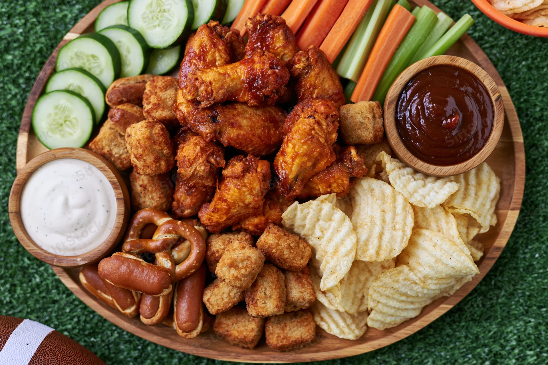 Wooden snack board with chicken wings, chips, vegetables and dips arranged for game day