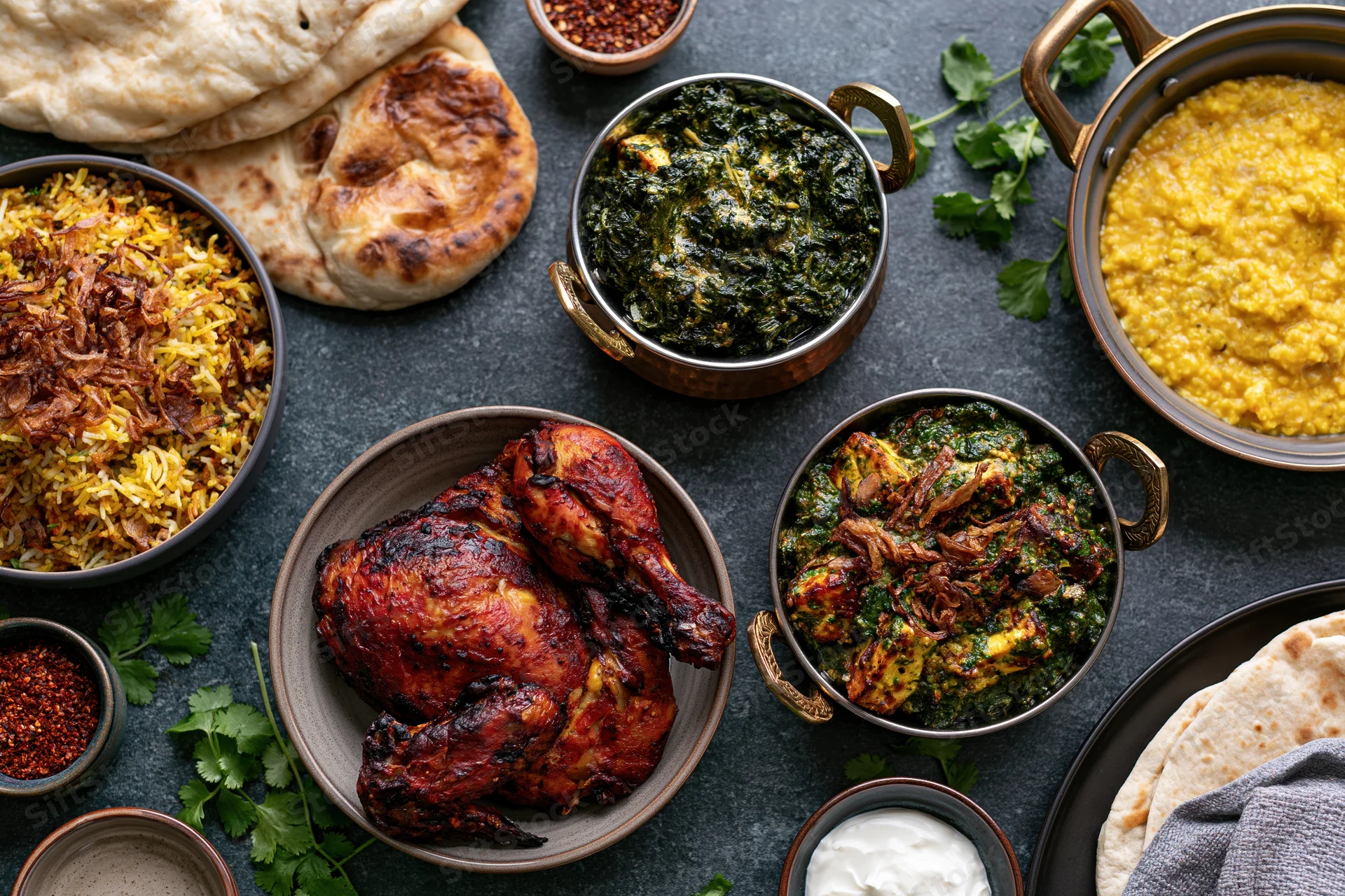 Indian feast spread with tandoori chicken, palak paneer, dal, rice, naan and yogurt on dark surface
