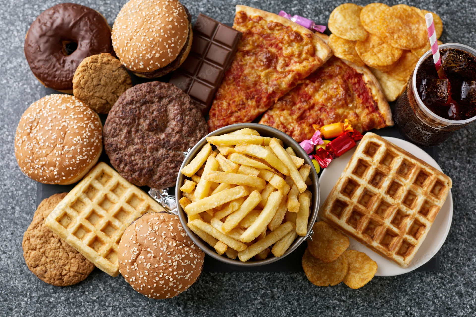 Overhead flat lay of assorted junk food spread across a dark surface