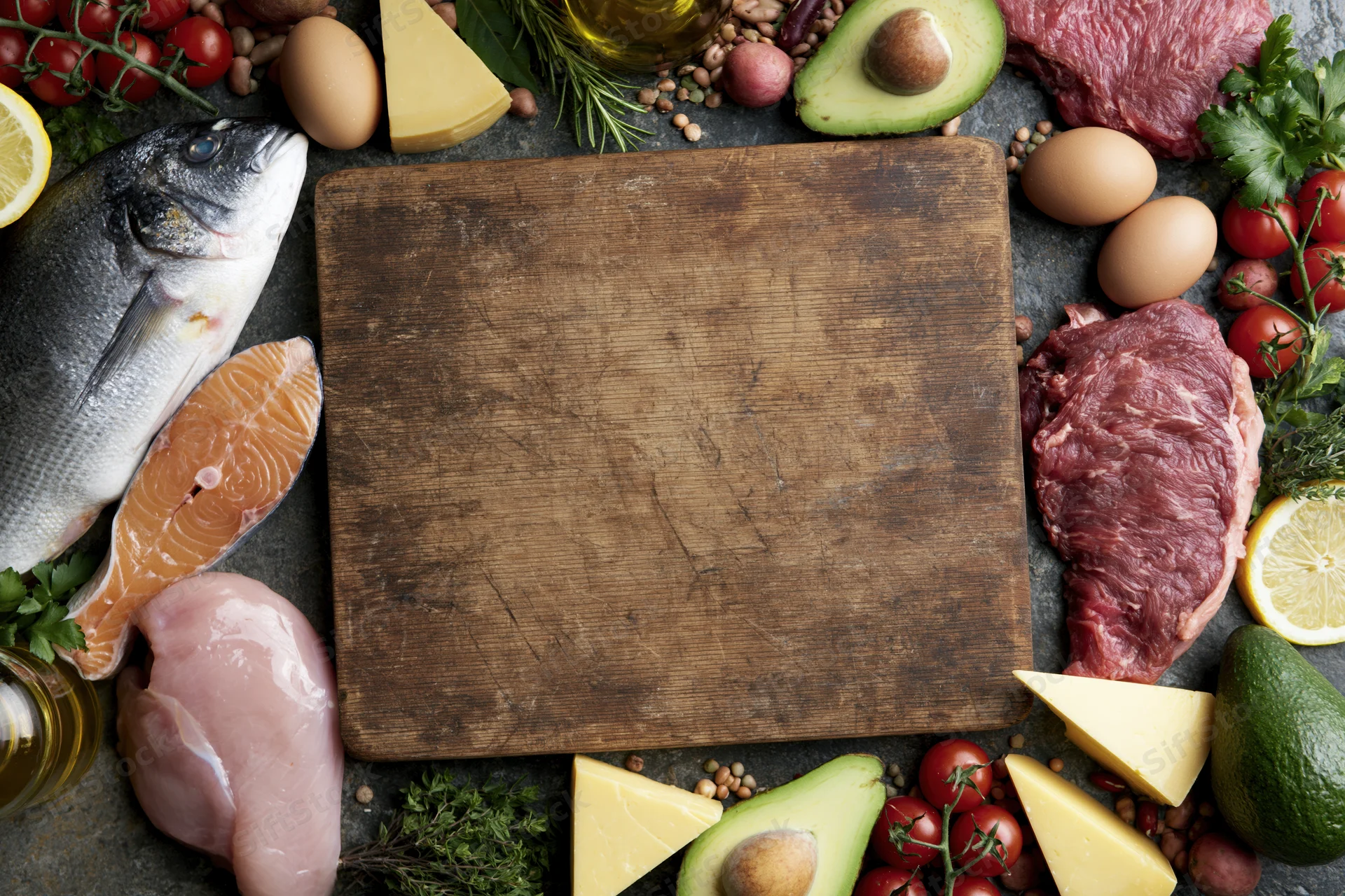Empty worn wooden cutting board surrounded by raw food ingredients for meal preparation