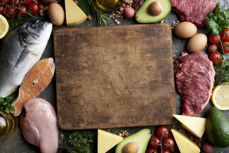 Empty worn wooden cutting board surrounded by raw food ingredients for meal preparation