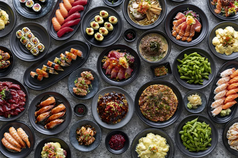 Overhead flat lay of an extensive japanese restaurant spread with multiple dishes arranged on black plates
