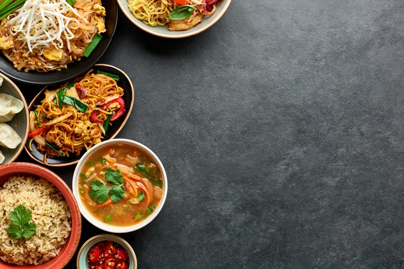 Assorted asian dishes arranged along the left side of a dark surface in overhead flat lay view