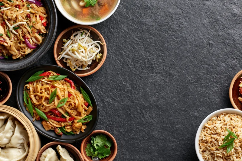 Assorted asian dishes arranged in bowls and plates on a dark slate surface with copyspace