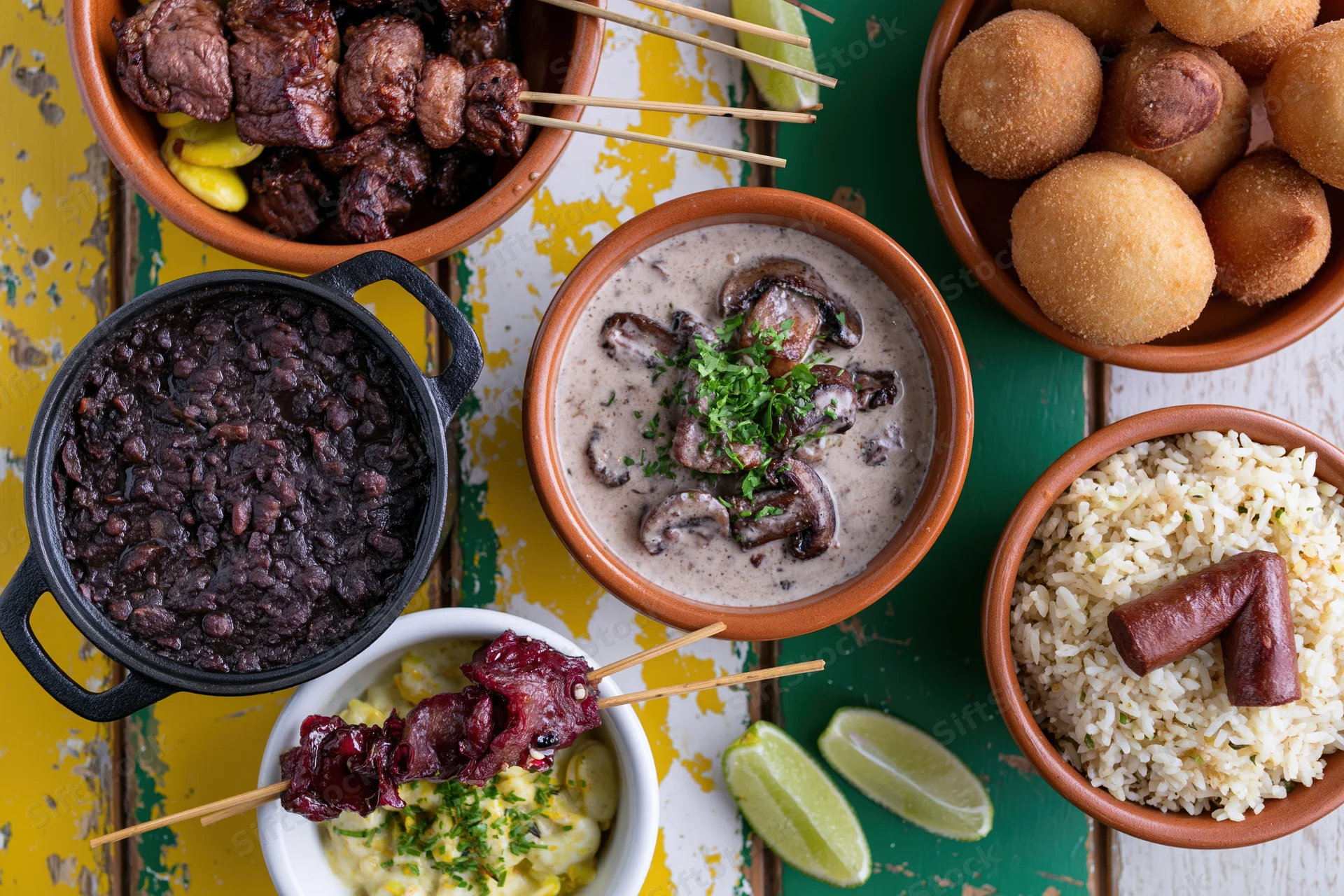 Assorted brazilian dishes arranged in bowls and skewers on a colorful wooden surface