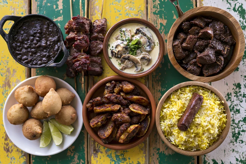 Assorted brazilian dishes arranged on a distressed yellow and green wooden table in overhead flat lay view
