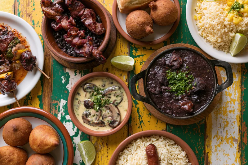 Assorted brazilian dishes arranged on a rustic painted wooden table in overhead flat lay view