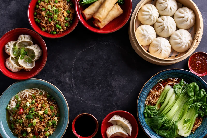 Overhead flat lay of assorted chinese dishes arranged in a circle on dark surface with copyspace in center