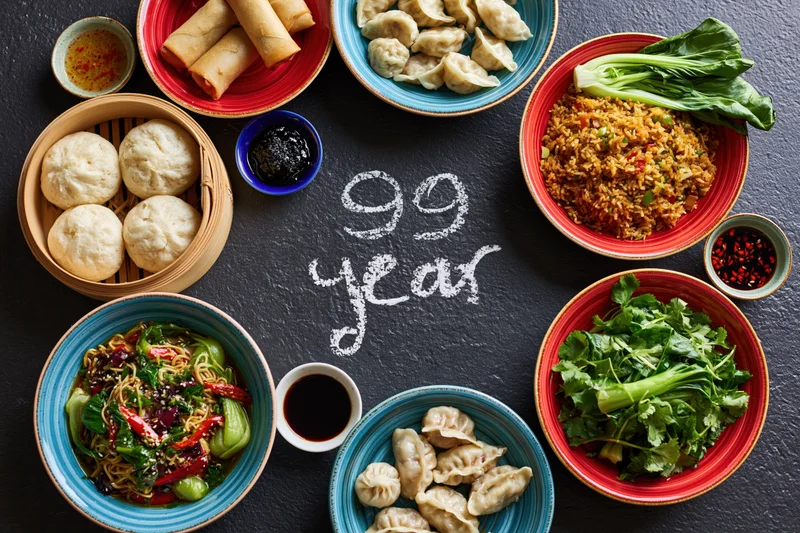 Assorted chinese dishes arranged in a circle around chalk-written 99 year on dark slate surface