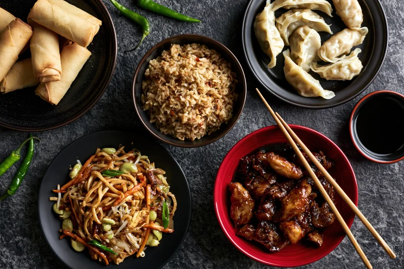 Overhead flat lay of assorted chinese dishes arranged on dark stone surface with chopsticks and sauces