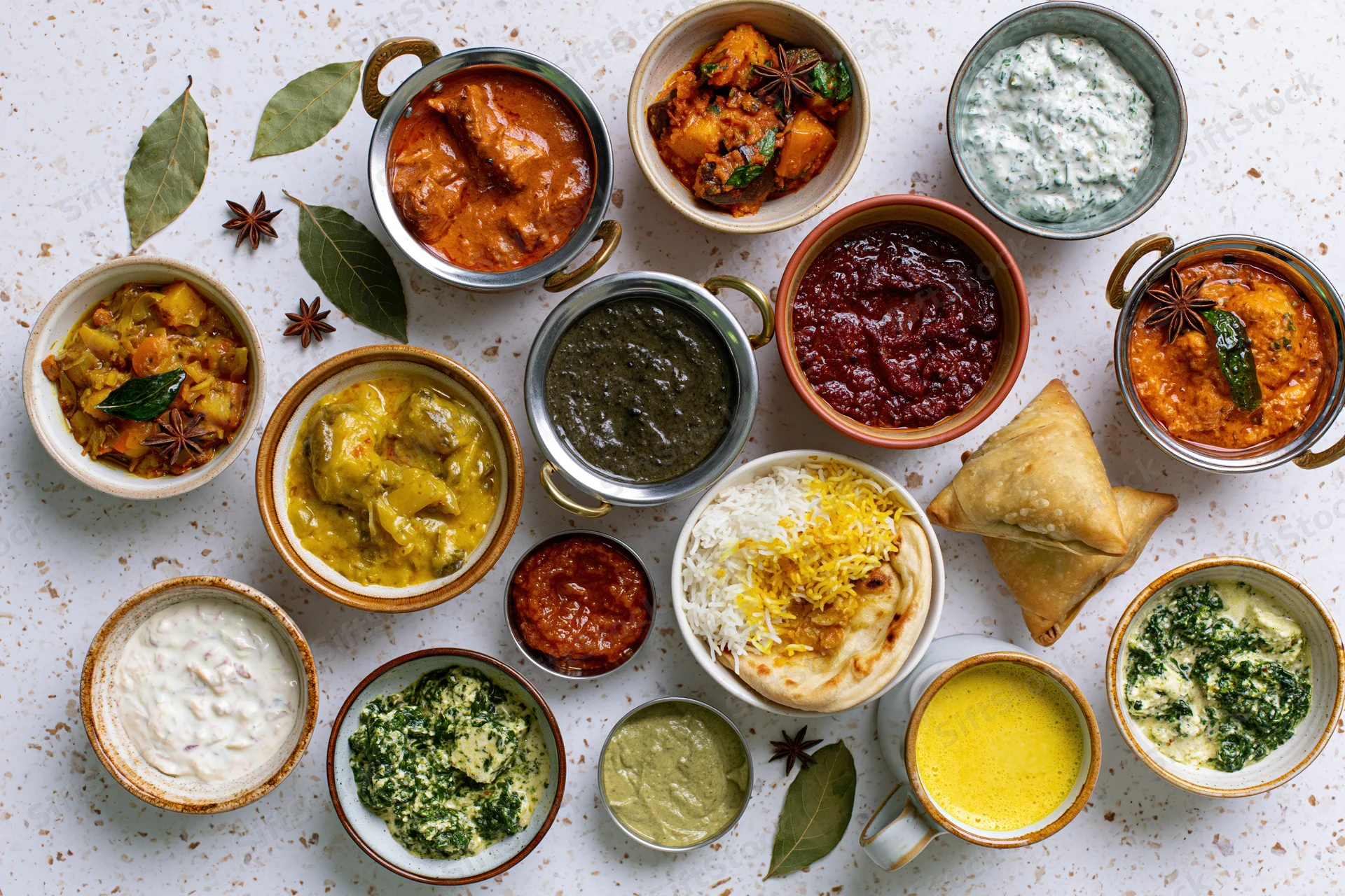 Overhead flat lay of assorted Indian dishes arranged on a speckled white surface