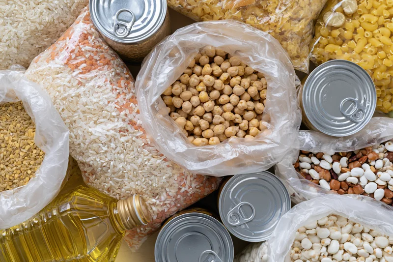 Overhead flat lay of assorted dry pantry staples and canned goods arranged on a surface