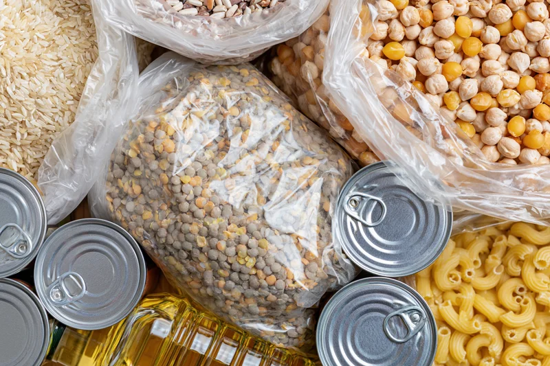 Overhead flat lay of assorted dry pantry staples and canned goods arranged on a surface