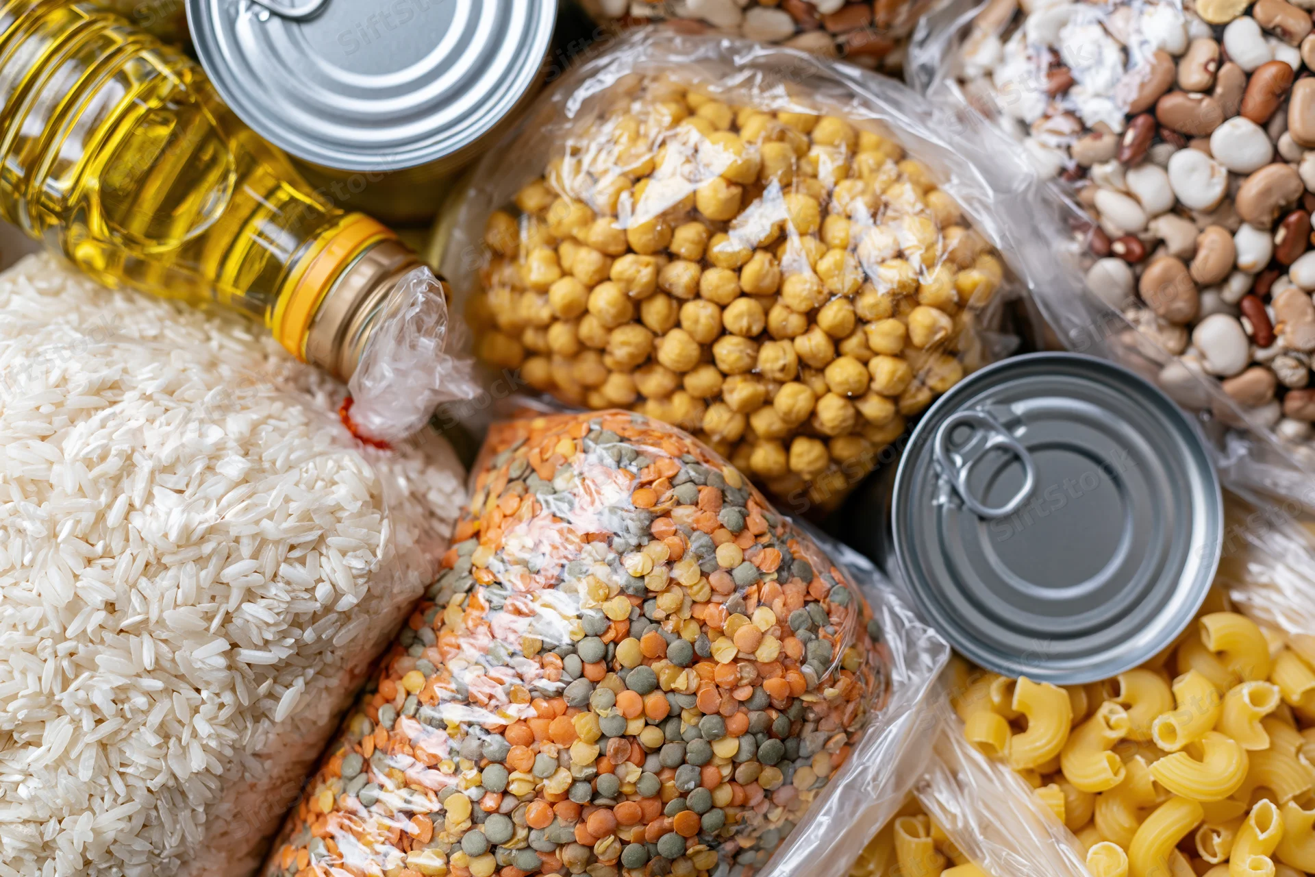 Overhead flat lay of assorted dry pantry staples and canned goods arranged on a surface
