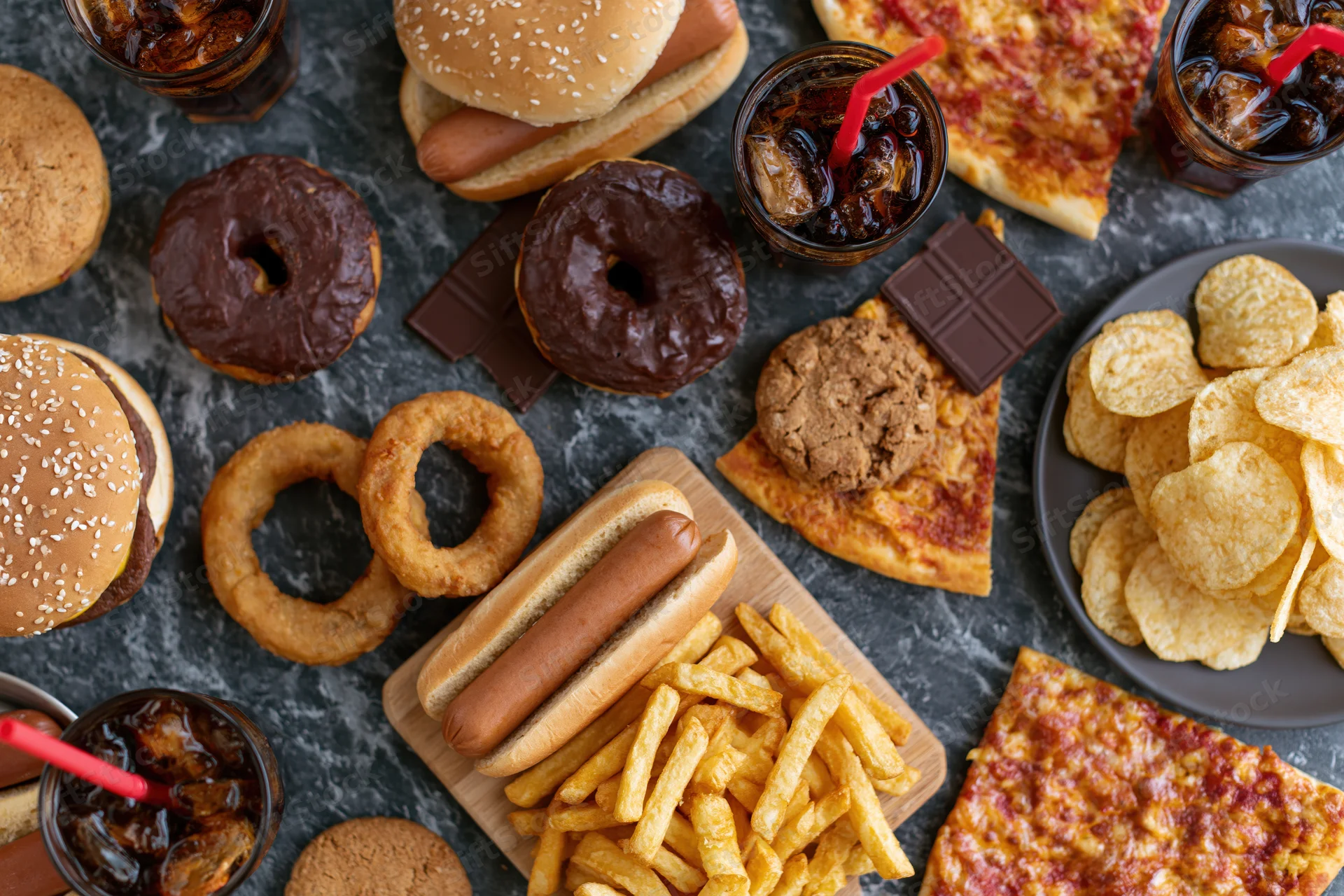 Overhead flat lay of assorted fast food and junk food spread on dark surface