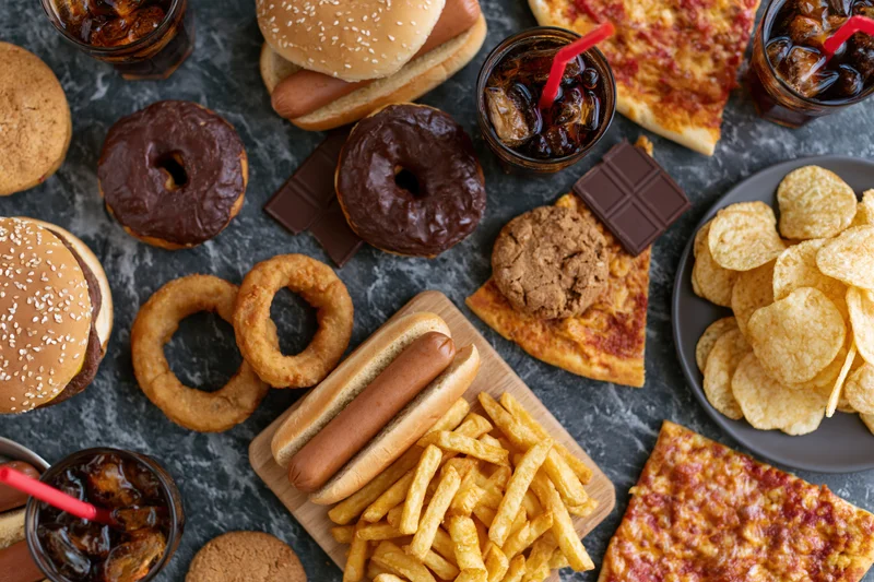 Overhead flat lay of assorted fast food and junk food spread on dark surface