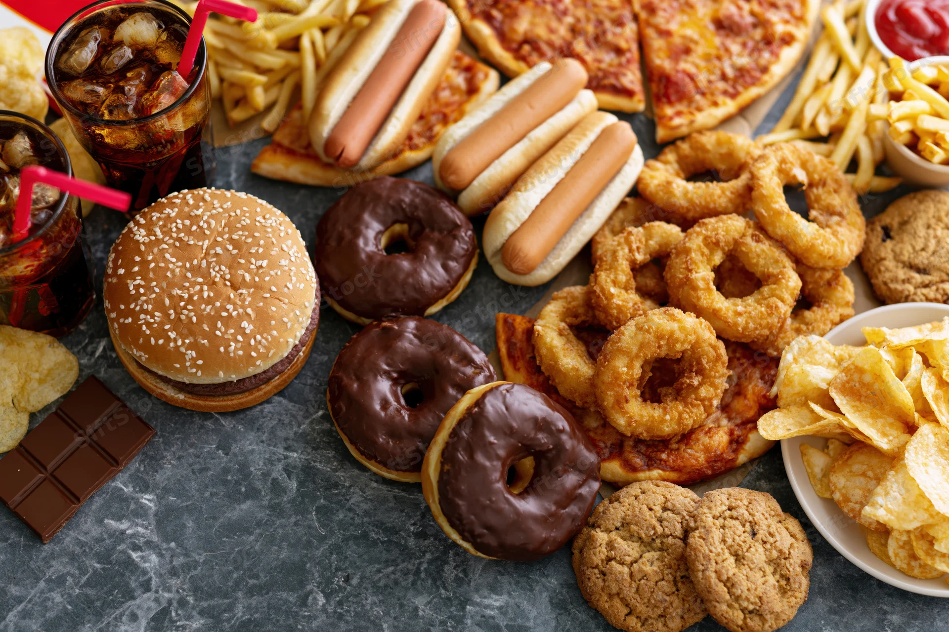 Overhead flat lay of assorted fast food and junk food spread on dark surface
