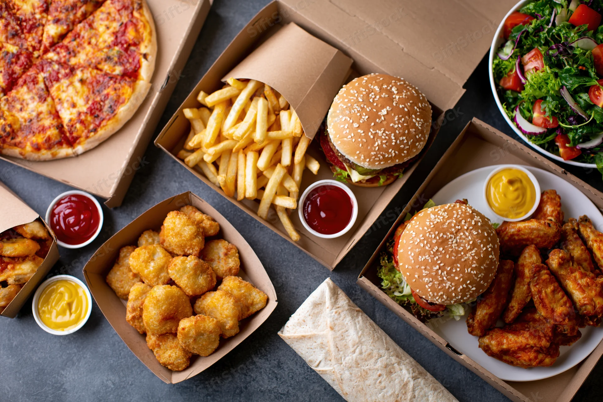 Assorted fast food items arranged in cardboard boxes and bowls on a dark surface
