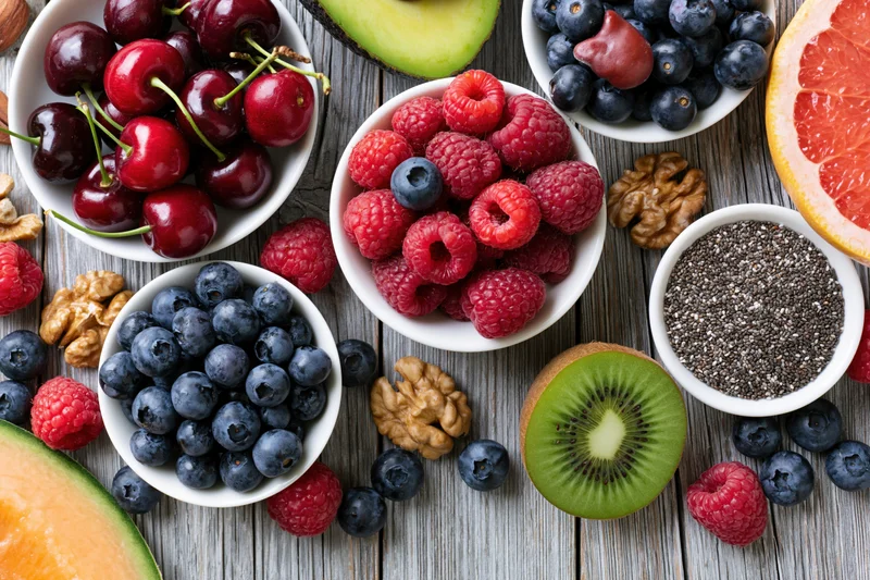 Overhead flat lay of assorted fresh fruits berries nuts and chia seeds on wooden table