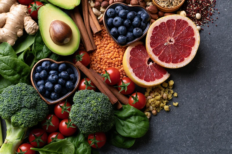 Overhead flat lay of fresh vegetables fruits and grains arranged on dark slate surface