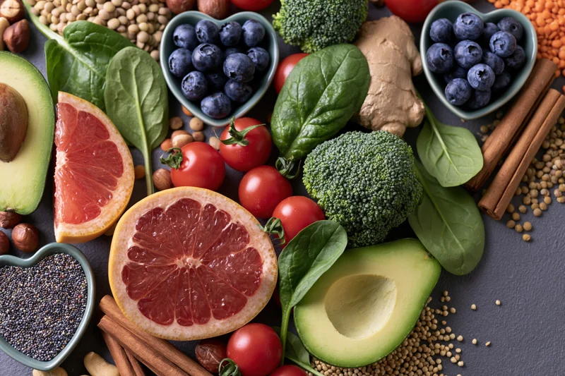 Overhead flat lay of fresh fruits vegetables grains and spices arranged on dark surface
