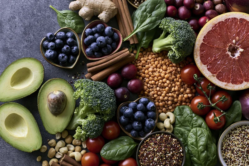 Overhead flat lay of fresh fruits vegetables grains and nuts arranged on dark surface