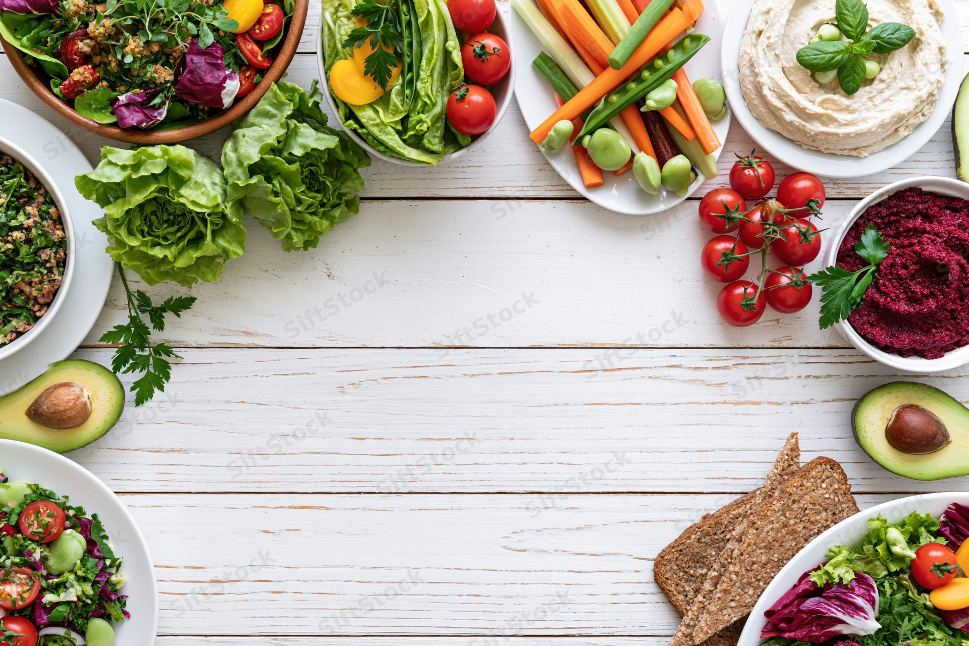 Overhead flat lay of assorted healthy vegetarian dishes and snacks arranged around a white wooden table with central copyspace