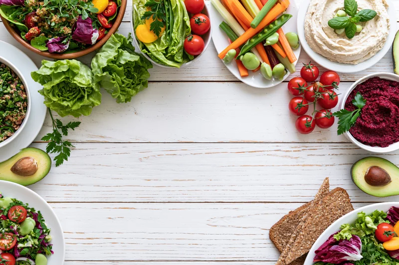 Overhead flat lay of assorted healthy vegetarian dishes and snacks arranged around a white wooden table with central copyspace